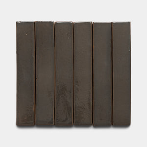 Six Zia Tile Cacao Mini Bar tiles, dark brown and rectangular, are arranged vertically in a row on a plain white background, creating a simple and uniform look.