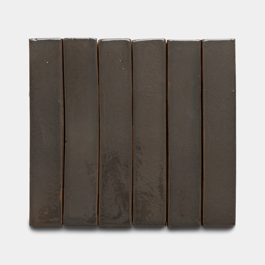 Six Zia Tile Cacao Mini Bar tiles, dark brown and rectangular, are arranged vertically in a row on a plain white background, creating a simple and uniform look.