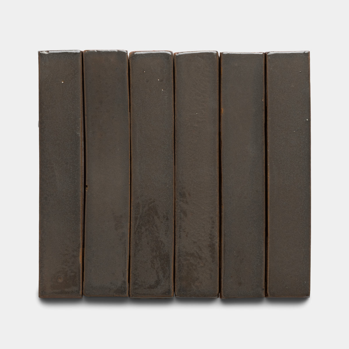Six Zia Tile Cacao Mini Bar tiles, dark brown and rectangular, are arranged vertically in a row on a plain white background, creating a simple and uniform look.