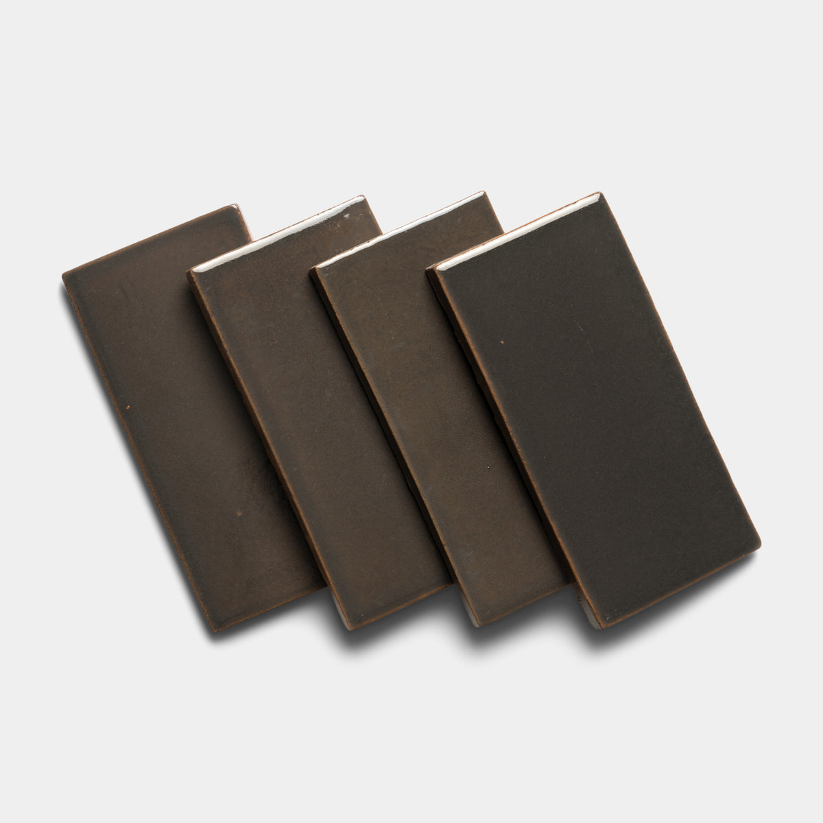Four Zia Tile Cacao 4x8 Rectangle ceramic tiles, in dark brown, are arranged in an overlapping, slightly fanned-out pattern on a light gray background.