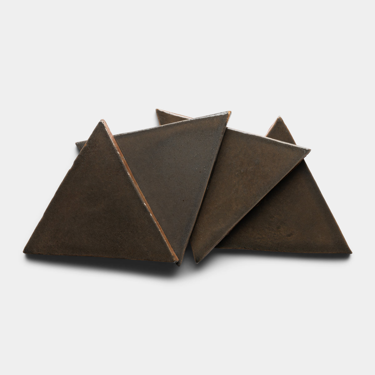 Four Cacao Triangle tiles by Zia Tile, made of dark ceramic, are arranged in a layered, overlapping triangular pattern on a white background.