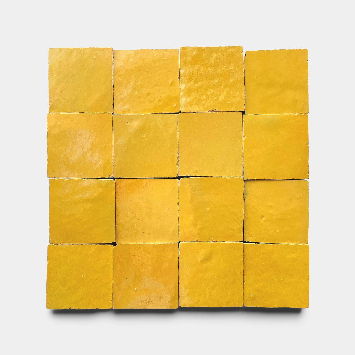 A grid of sixteen Cadmium 2x6 handmade yellow tiles by Zia Tile, arranged in four rows and four columns on a plain light gray background.