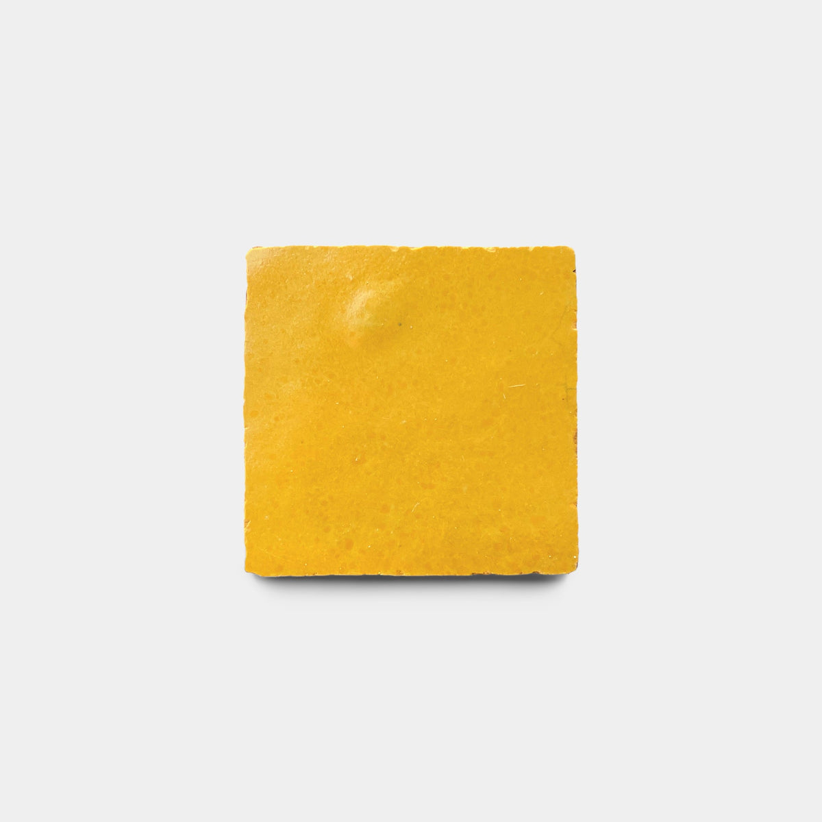 A single, square, yellow Cadmium 2x2 sample tile by Zia Tile with a slightly rough texture is centered on a plain white background, echoing the look of a handmade tile.