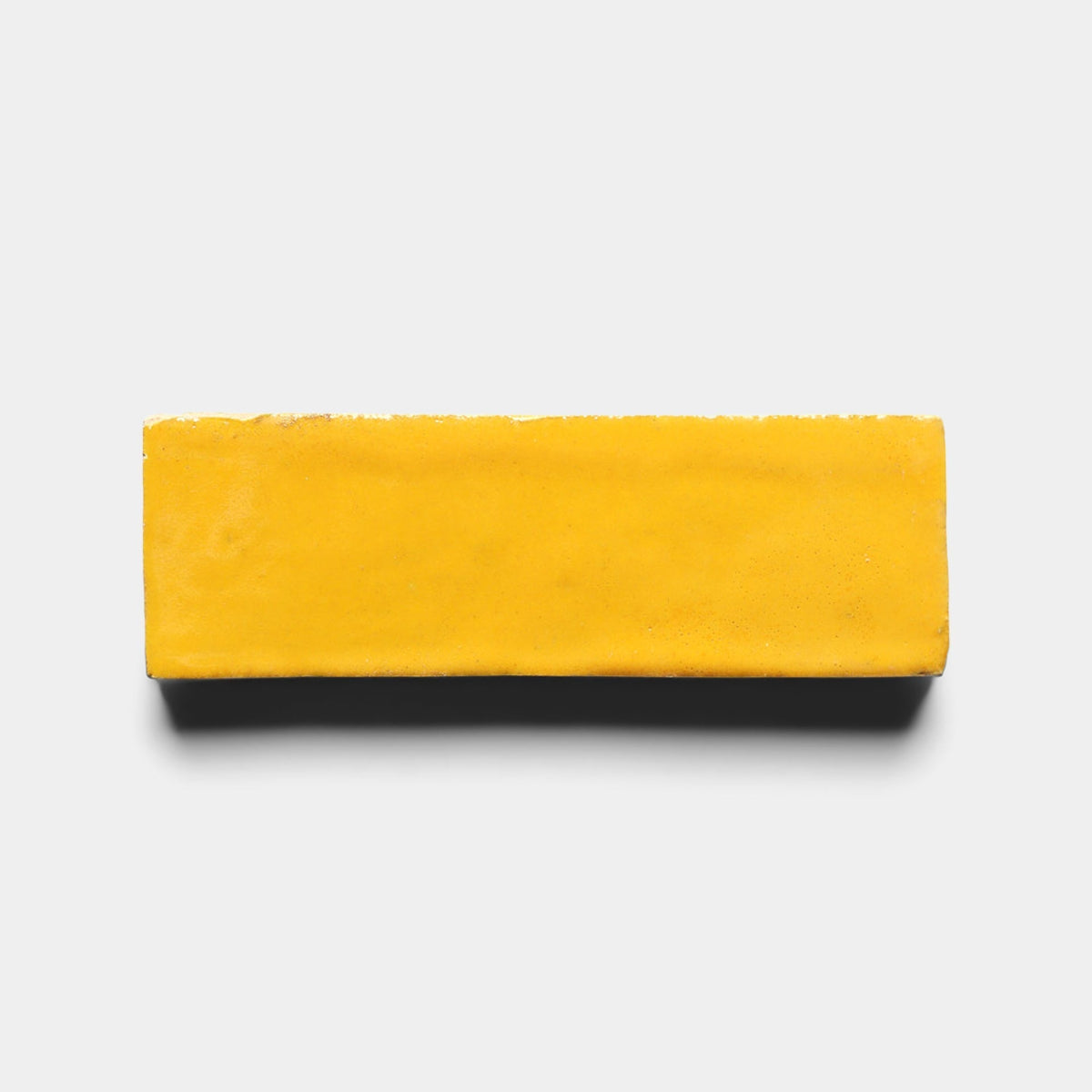 A single Cadmium 2x6 sample tile by Zia Tile, rectangular and yellow, is centered on a plain light gray background with a soft shadow beneath it.
