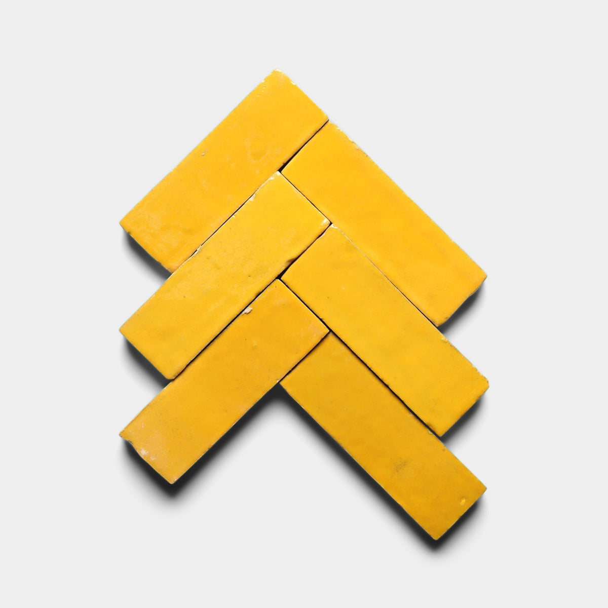 Six Cadmium 2x6 sample tiles by Zia Tile are arranged on a white background in a geometric, upward-pointing arrow pattern, reminiscent of bold handmade tile designs, with shadows adding depth.