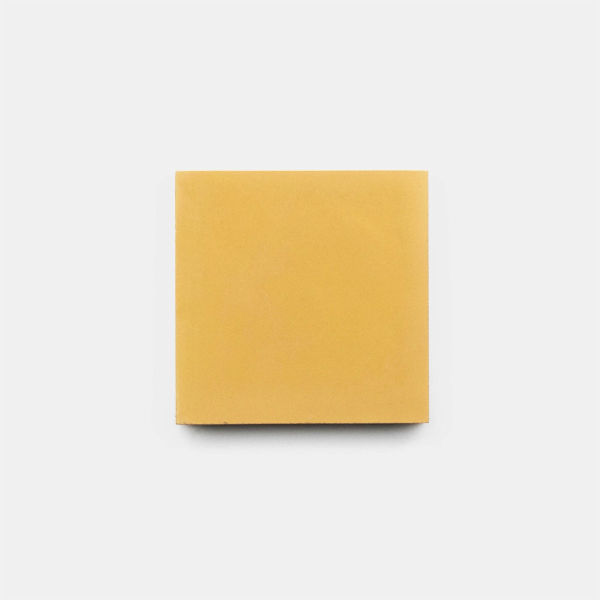 A single slice of yellow processed cheese sits centered on a plain white background, echoing the simple elegance of Zia Tile’s Cadmium 2x6 sample.