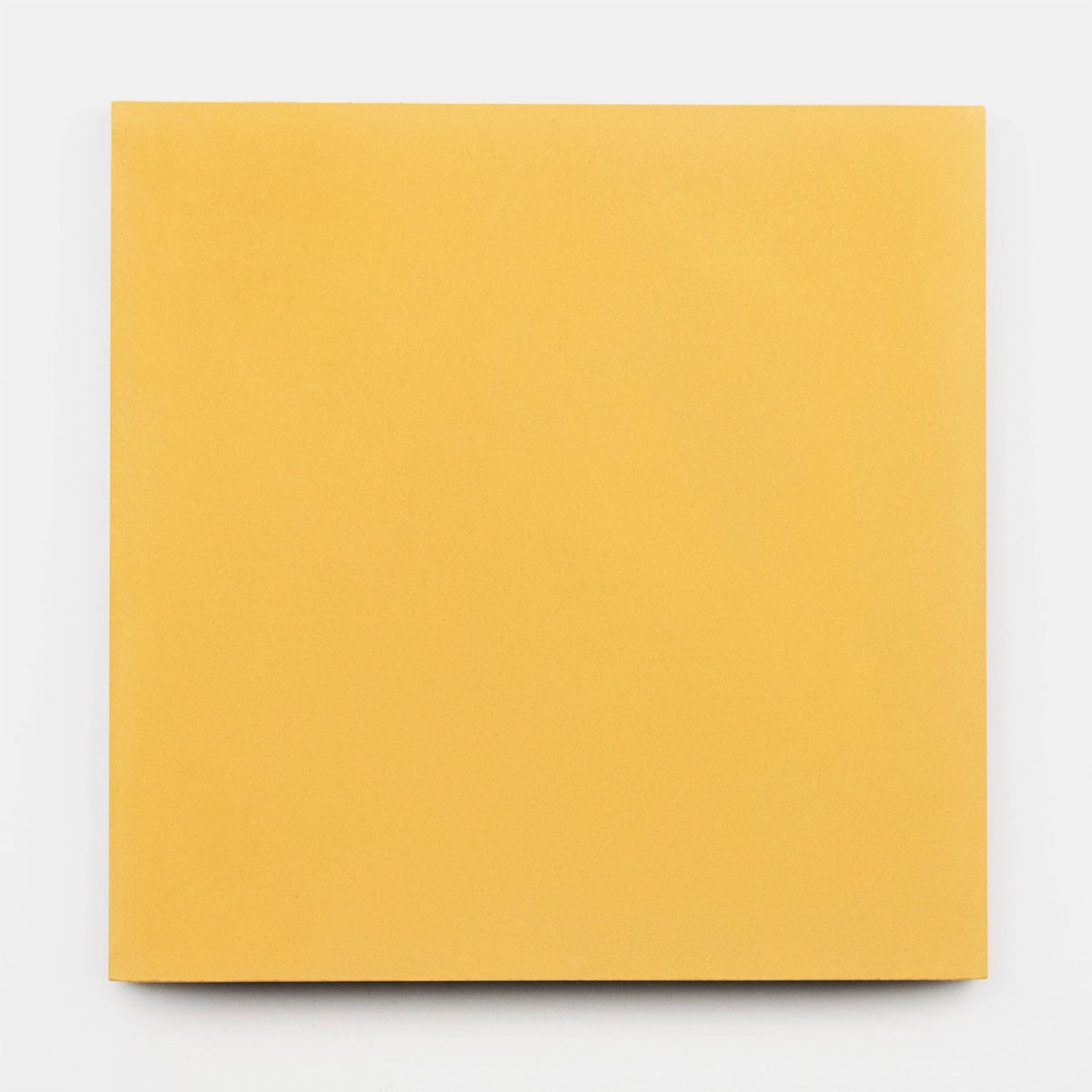 A simple, square, plain yellow book or notebook sits on a white background, evoking the clean, minimalist aesthetic of Zia Tile’s Cadmium 2x6 sample.
