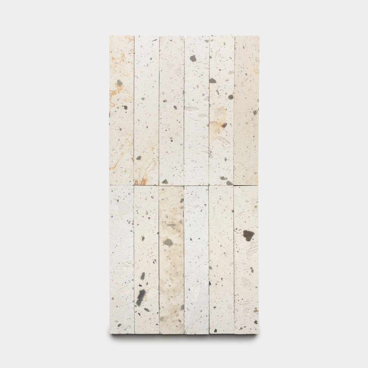 Caldera 2x12 by Zia Tile features rectangular tiles in cream and beige hues with a speckled pattern of gray and brown, arranged vertically or horizontally on a plain white background.