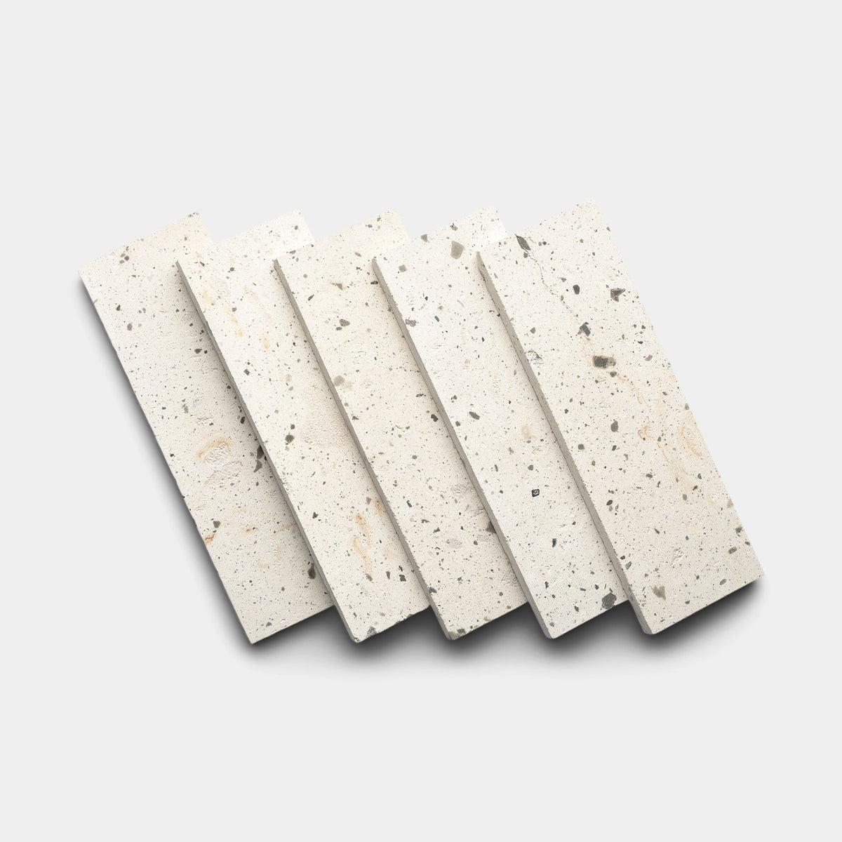 Five rectangular terrazzo tiles with a white base and scattered gray and beige speckles are arranged in a fanned-out pattern on a light gray background.