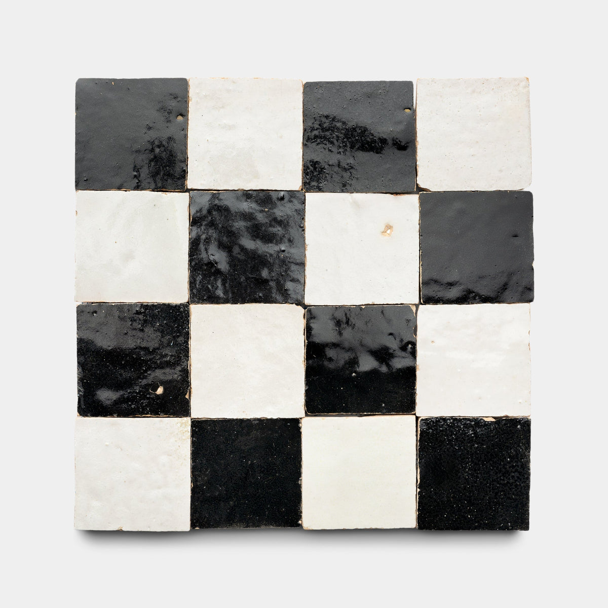 A square tile mosaic featuring Zia Tile’s Carbon Black + Casablanca Checkerboard sample, arranged in a 4x4 pattern of alternating glossy black and white cement tiles on a light gray background.