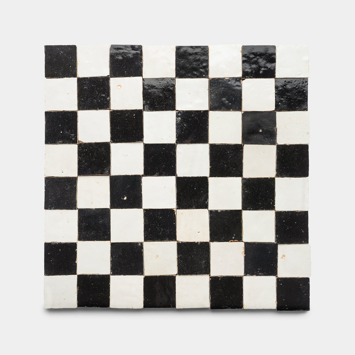 The Carbon Black + Casablanca Checkerboard sample by Zia Tile features a glossy black and white square ceramic tile with an artisanal, slightly uneven handmade surface and an alternating checkerboard grid pattern.
