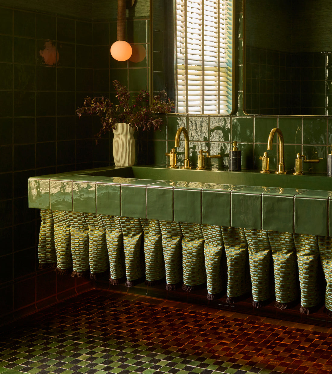A vanity featuring a green 2x2 zellige tiled countertop and a fringe skirt, set against dark green tiled walls and a Carbon Black + Racing Green Checkerboard floor.