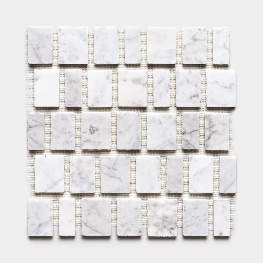 A grid of Scarpa in Carrara sample tiles by Zia Tile, featuring rectangular white marble with subtle gray veining, is evenly arranged on mesh backing and shown against a plain white background.
