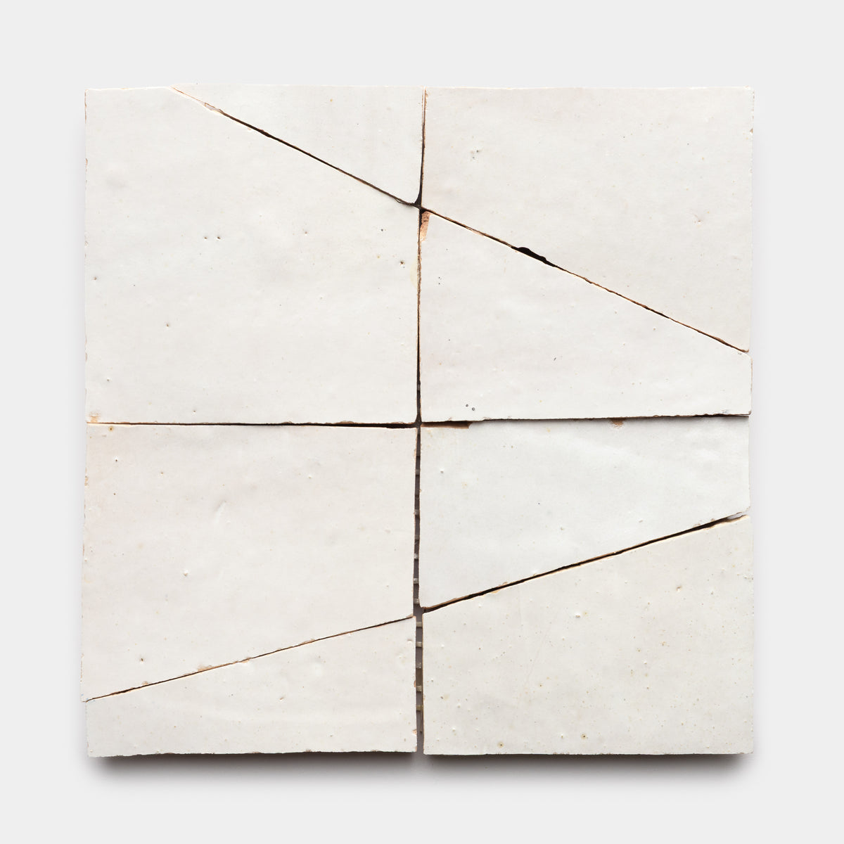 The Atlas 5 by Zia Tile features four off-white ceramic tiles arranged in a square, each slightly misaligned with visible diagonal and vertical cracks that create an irregular, fragmented pattern on a plain background.