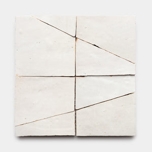 The Atlas 5 by Zia Tile features four off-white ceramic tiles arranged in a square, each slightly misaligned with visible diagonal and vertical cracks that create an irregular, fragmented pattern on a plain background.