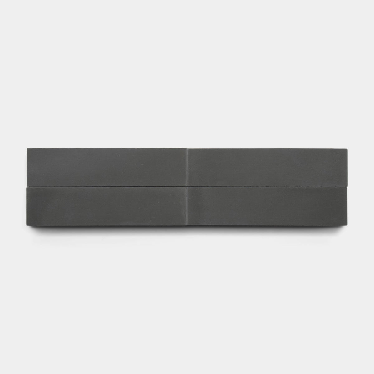 The Charcoal 2x8 Sample by vendor-unknown features four smooth, dark gray rectangular blocks in a row on light gray, separated by subtle lines—evoking minimalist sculpture and handmade tile design.