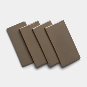 Four Condesa 4x8 Rectangle tiles by Zia Tile, in brown ceramic, are arranged in a slightly fanned-out stack on a white background, each tile overlapping the next and casting soft shadows.