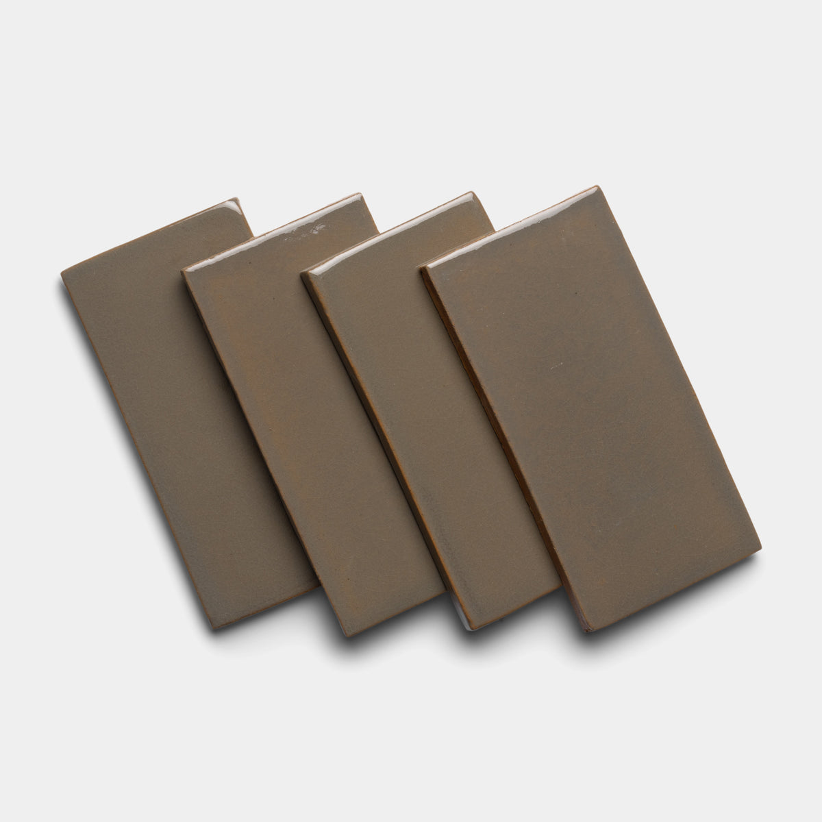 Four Condesa 4x8 Rectangle tiles by Zia Tile, in brown ceramic, are arranged in a slightly fanned-out stack on a white background, each tile overlapping the next and casting soft shadows.