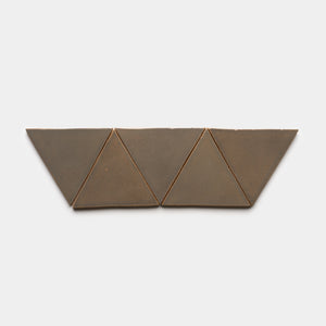 Four Condesa Triangle tiles by Zia Tile, in bronze color, are arranged side by side to create a horizontal geometric pattern on a plain white background.