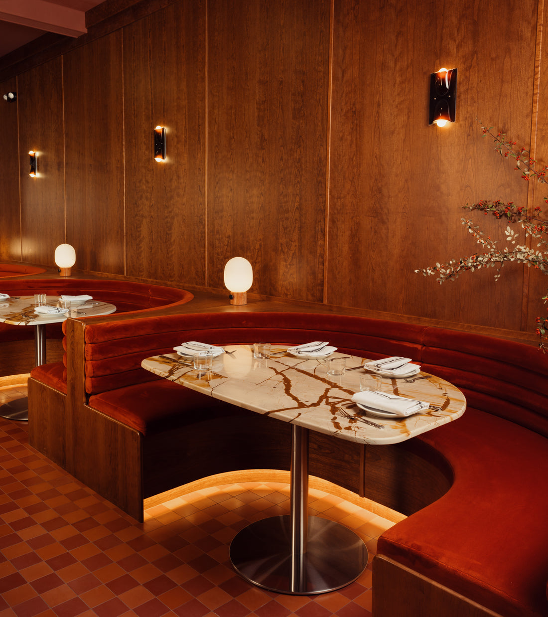 A curved red velvet booth, marble table for four, wood-paneled walls, soft lighting, and a vendor-unknown Coral 4x4 cement tile kitchen backsplash create a cozy and elegant dining space.