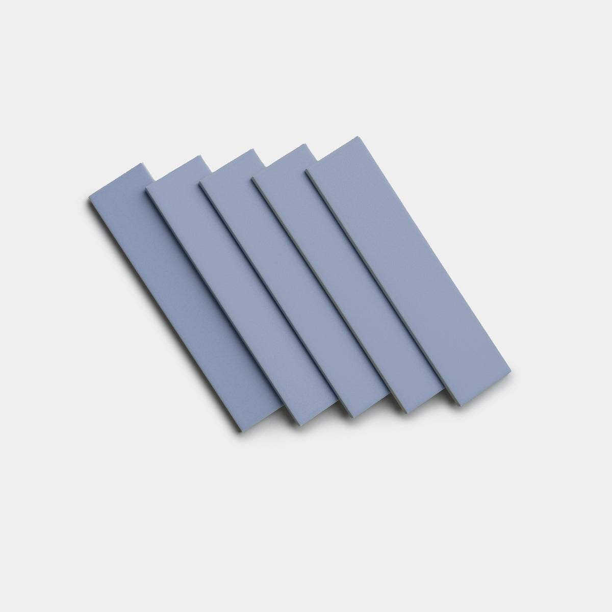 Five rectangular Cornflower 2x8 tiles by Zia Tile, in light blue, are arranged in a slightly fanned-out pattern on a plain white background.
