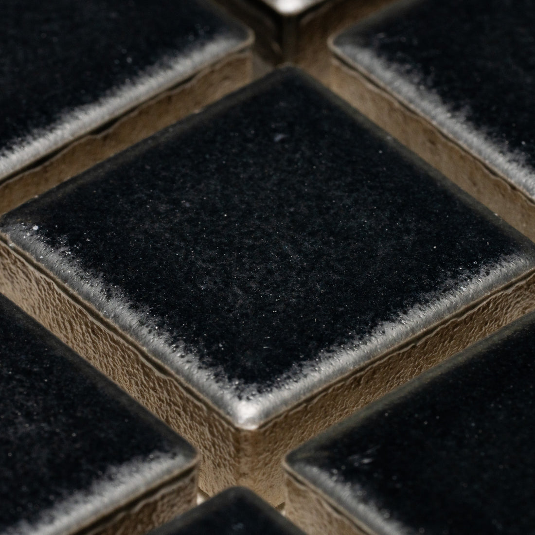 Close-up of Zia Tile’s Cosmic Black 1x1 tiles—shiny, square black tiles with metallic, slightly textured edges arranged in a grid.