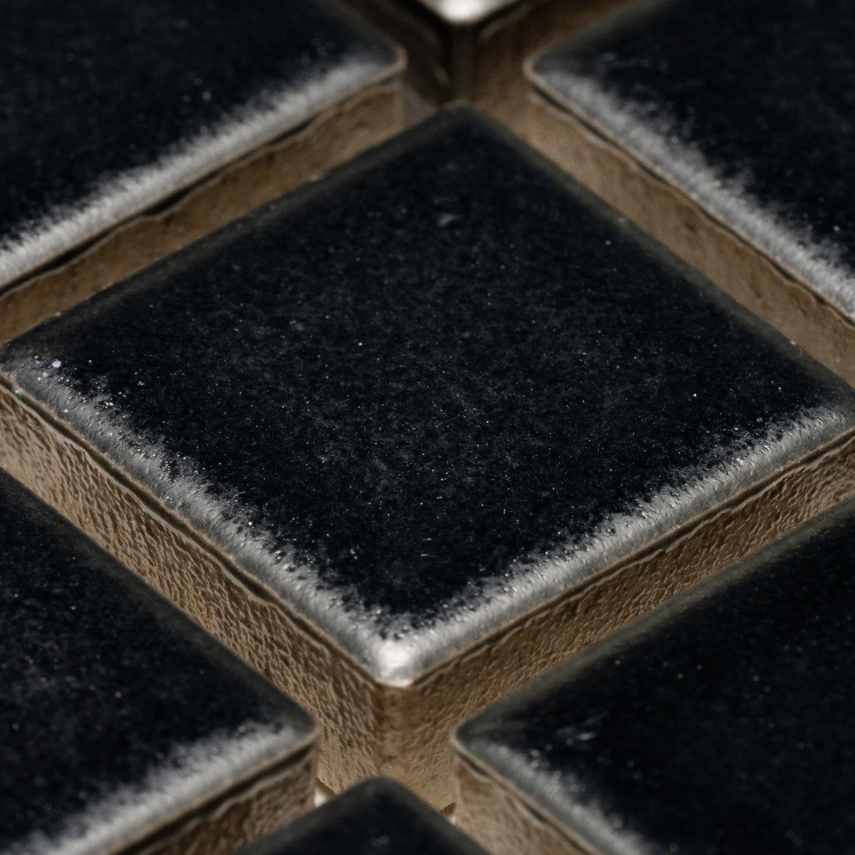 Close-up of Zia Tile’s Cosmic Black 1x1 tiles—shiny, square black tiles with metallic, slightly textured edges arranged in a grid.