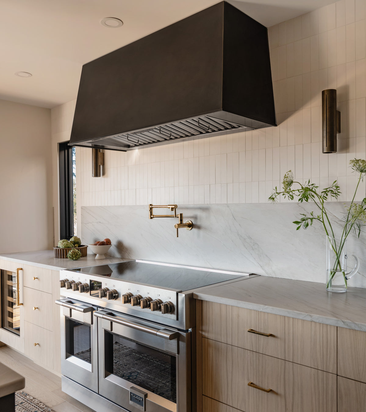 A modern kitchen featuring a stainless steel stove, black range hood, wooden cabinets, pot filler faucet, and decorative plants showcases a striking backsplash made of Cotton 2x8 subway tile by vendor-unknown.