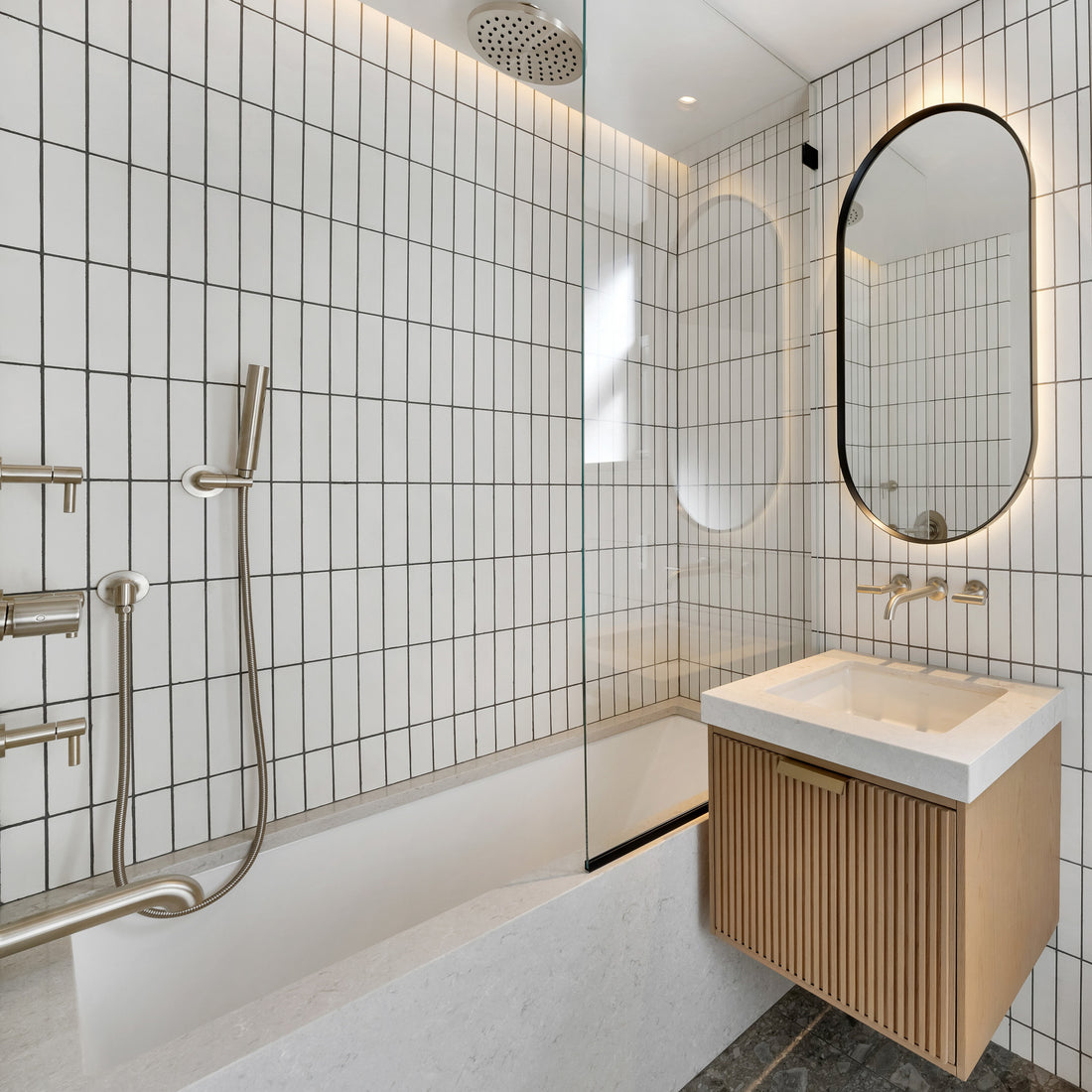 Modern bathroom with white rectangular tile walls, a shower with brushed metal fixtures, a bathtub, a floating wood vanity with a white countertop, an oval mirror, and built-in lighting above the mirror.