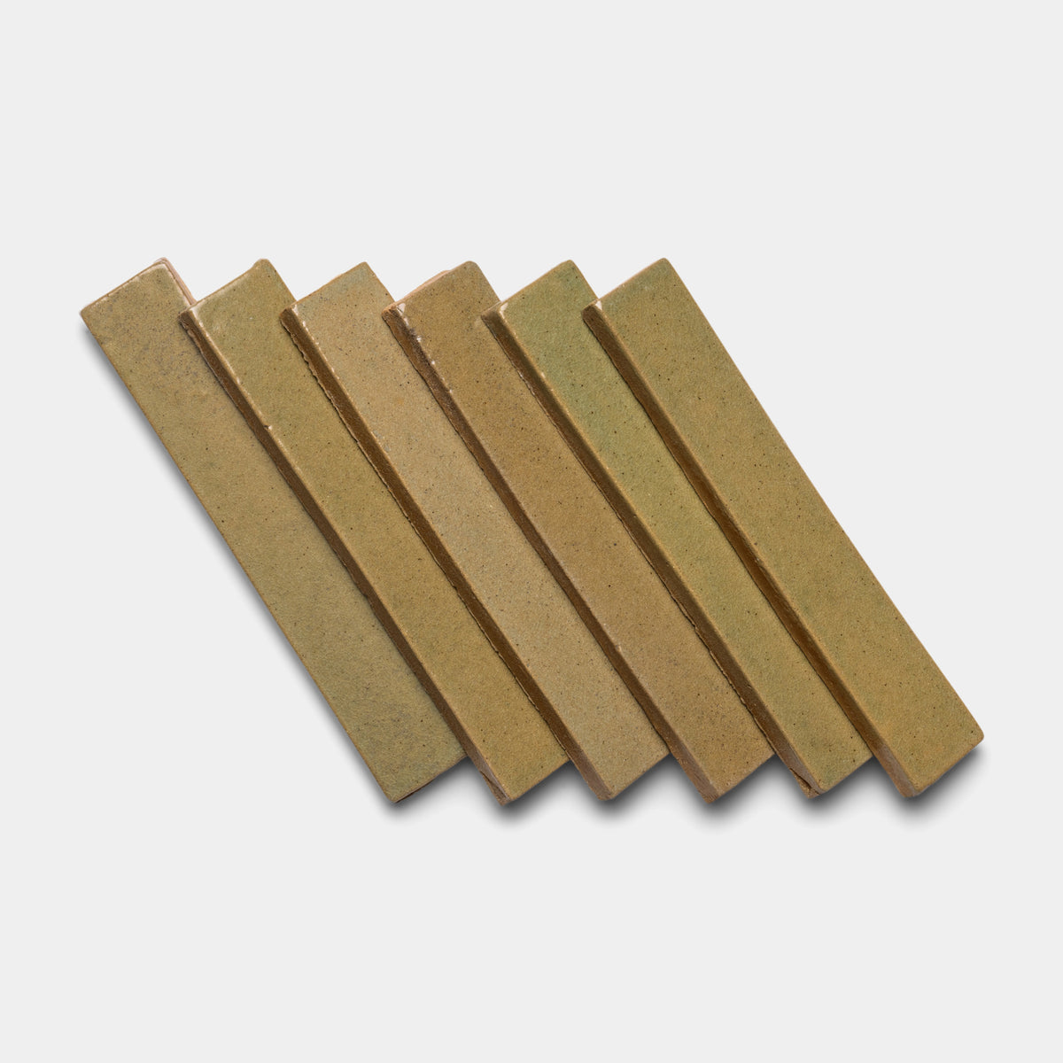 Six rectangular Creosote Mini Bar tiles by Zia Tile, in a light brown hue, are laid in a slanted, overlapping row on a white background.