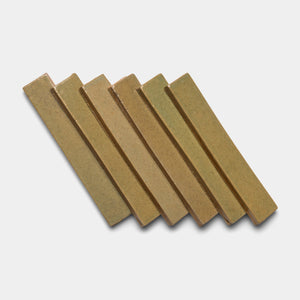 Six rectangular Creosote Mini Bar tiles by Zia Tile, in a light brown hue, are laid in a slanted, overlapping row on a white background.