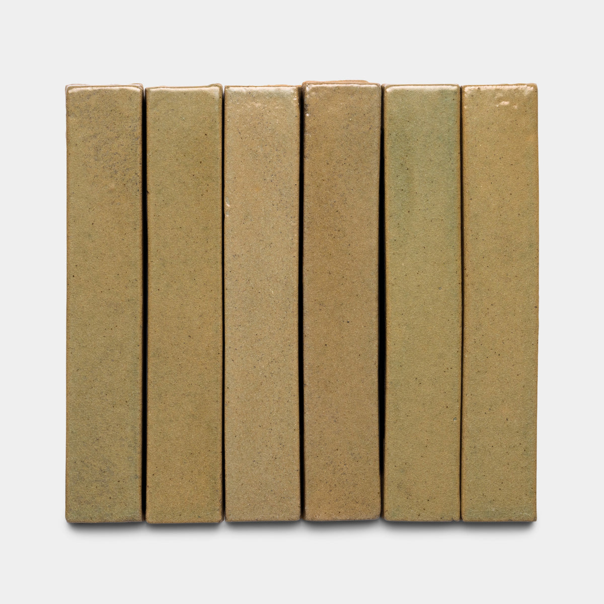 Six Creosote Mini Bar tiles by Zia Tile, rectangular and upright in tan, are aligned side by side against a plain light gray background. Their surfaces have a slightly rough, matte texture.