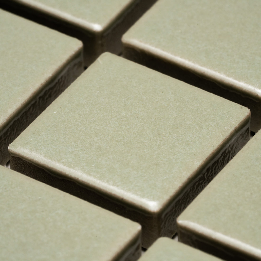 Close-up view of Cypress 1x1 square light green ceramic tiles by Zia Tile, arranged in a grid with visible grout lines.