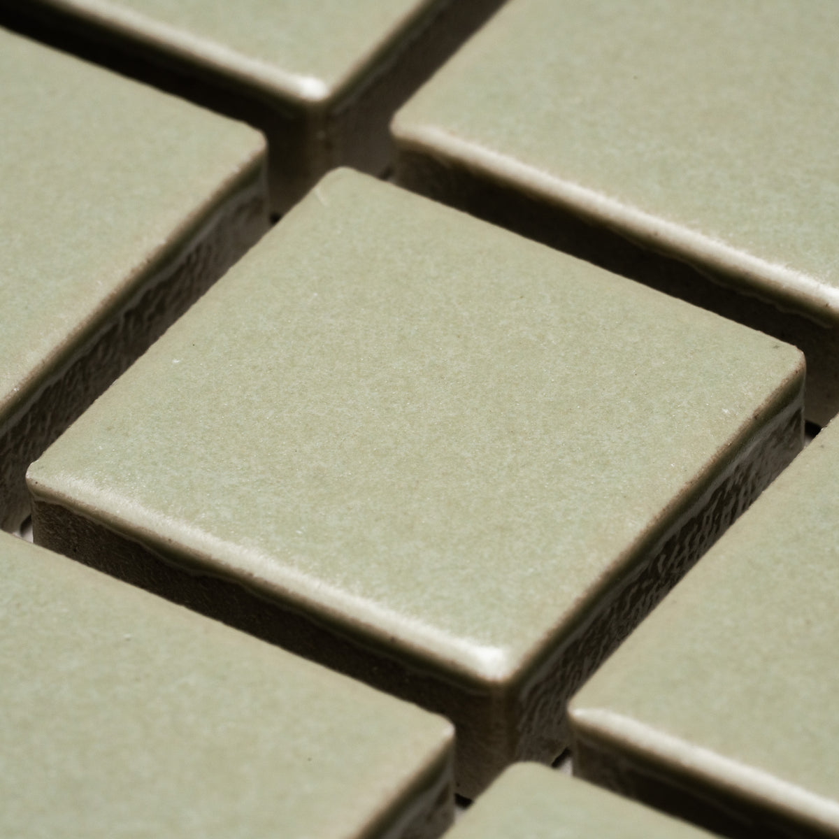 Close-up view of Cypress 1x1 square light green ceramic tiles by Zia Tile, arranged in a grid with visible grout lines.
