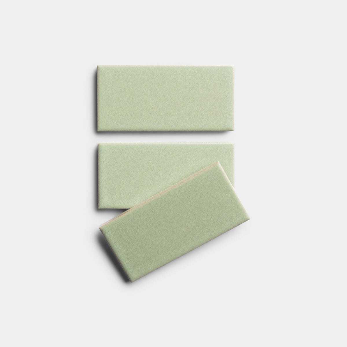 Three Cypress 2x4 sample tiles by Zia Tile in light green ceramic are arranged on a white background; two are stacked vertically, with the third tile placed diagonally across the bottom one.