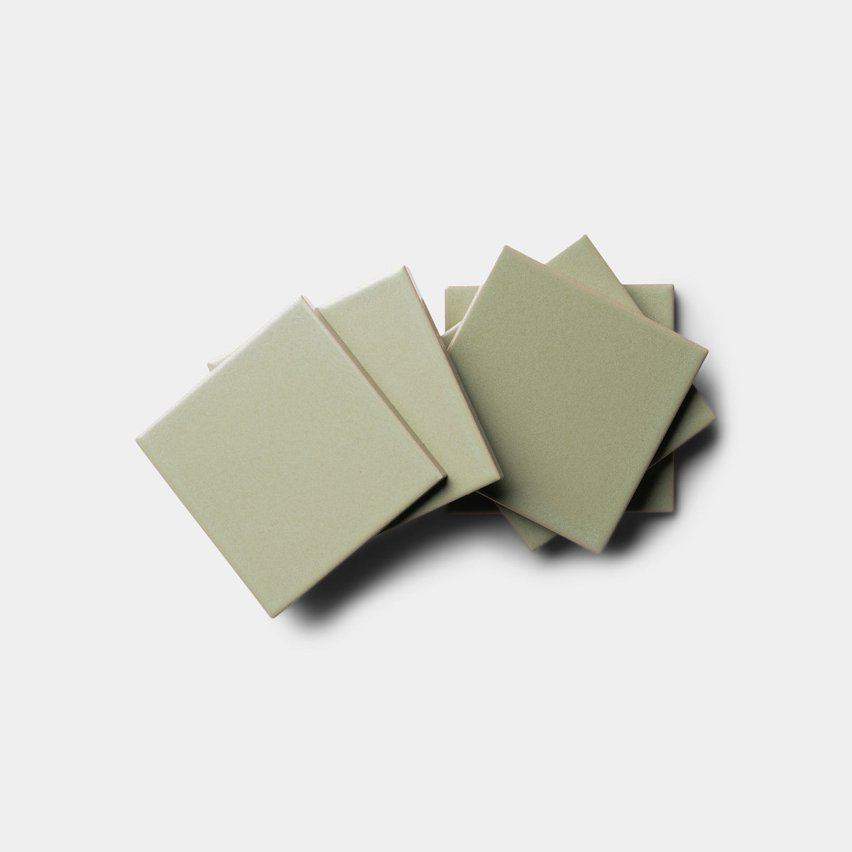 A stack of six Cypress 4x4 light beige square tiles from Zia Tile is arranged in a fan pattern on a white background, showing their smooth surfaces and sharp edges.