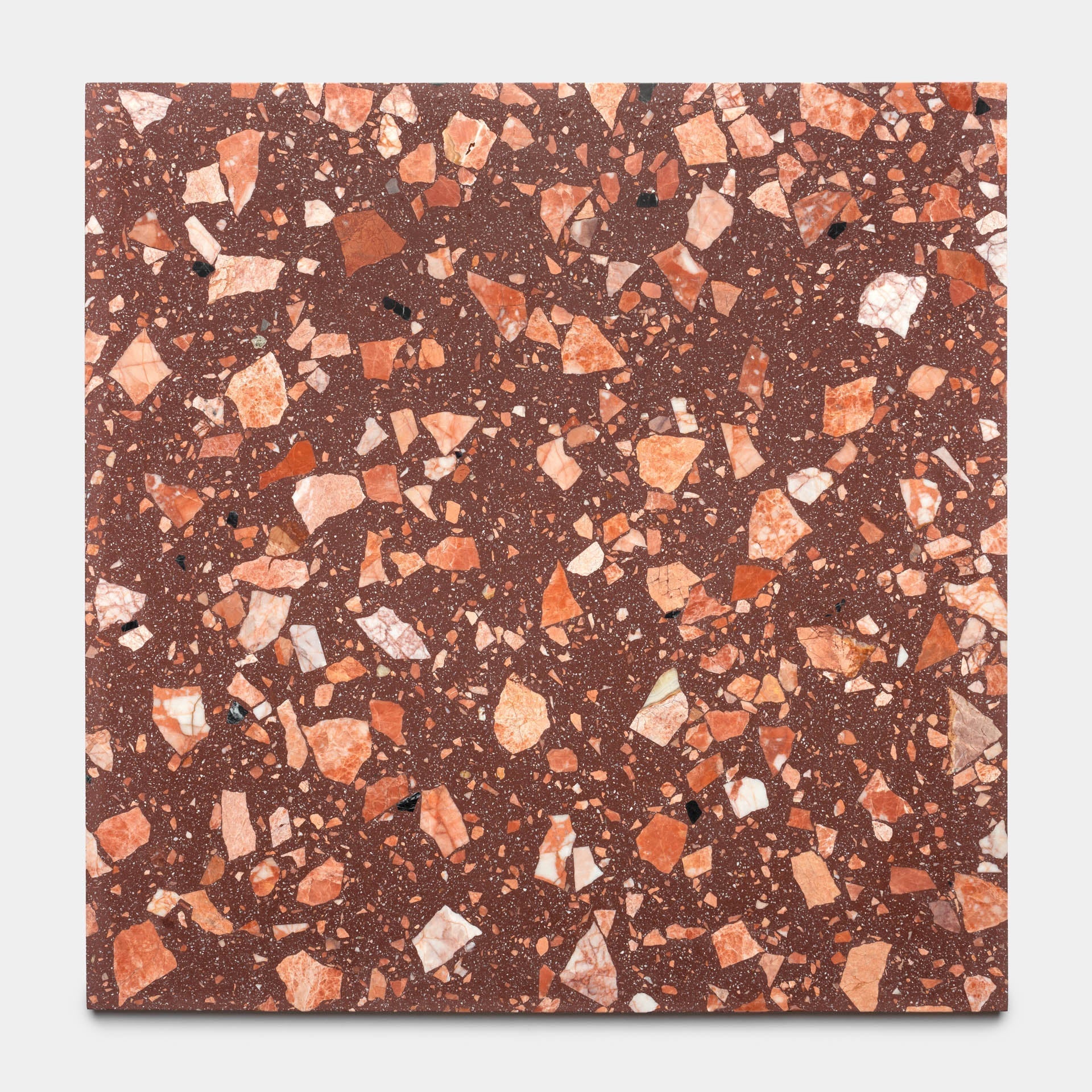 The Date Palm 24x24 by Zia Tile is a square, reddish-brown terrazzo tile featuring handcrafted design with irregular orange, pink, white, and black stone chips scattered across its surface.