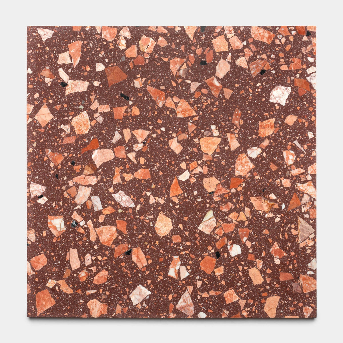The Date Palm 24x24 by Zia Tile is a square, reddish-brown terrazzo tile featuring handcrafted design with irregular orange, pink, white, and black stone chips scattered across its surface.