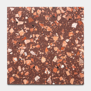 The Date Palm 24x24 by Zia Tile is a square, reddish-brown terrazzo tile featuring handcrafted design with irregular orange, pink, white, and black stone chips scattered across its surface.