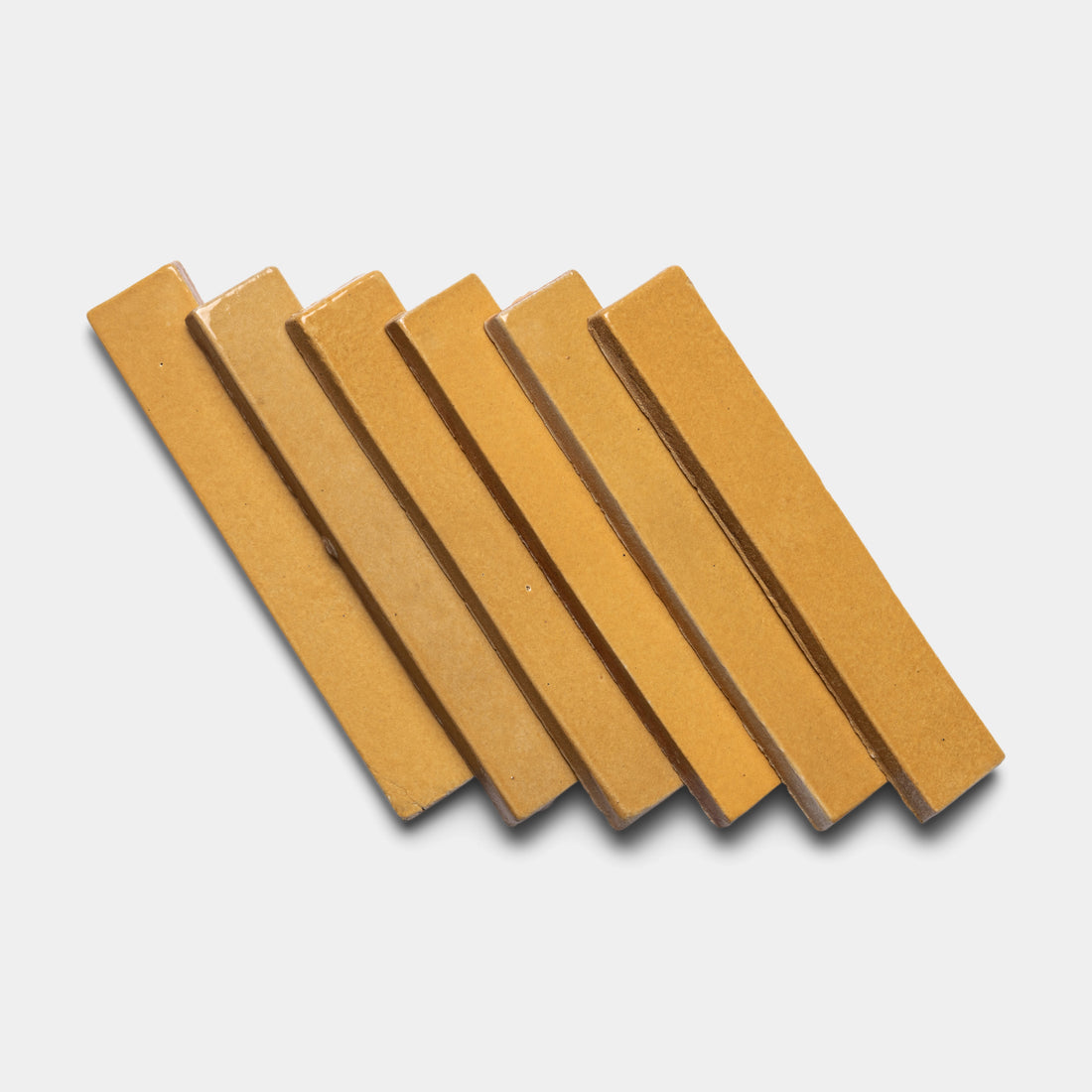 Six rectangular Dorado Mini Bars by Zia Tile, in a yellowish-brown shade, are arranged diagonally on a white background. The bars are evenly spaced with slight overlapping.