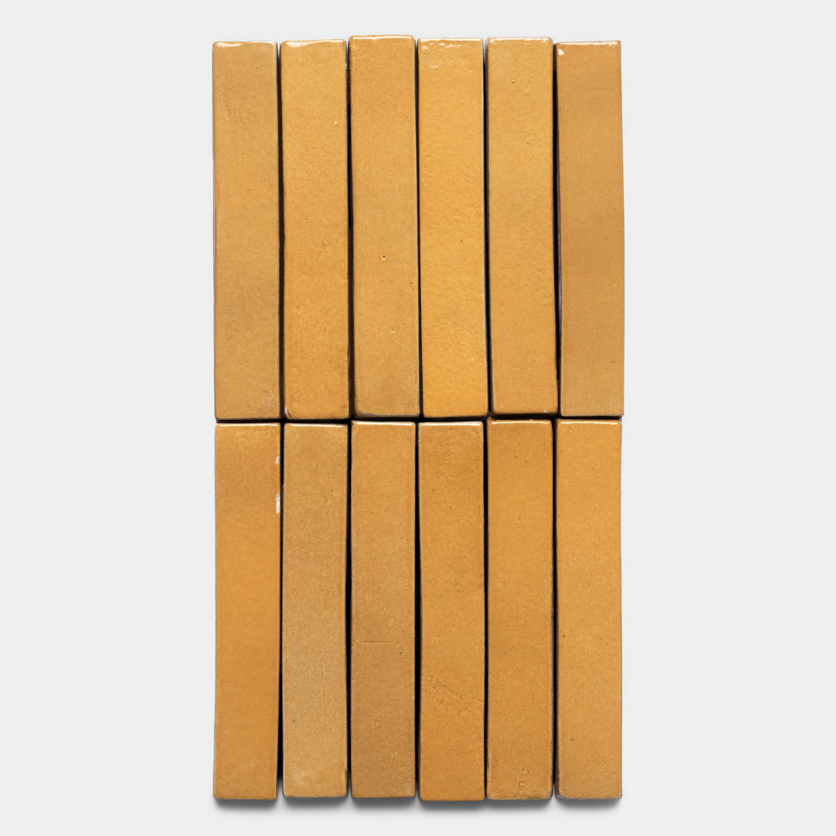 Twelve Dorado Mini Bar tiles by Zia Tile, in a rectangular yellowish-brown design, are arranged vertically in three rows of four, creating a neat grid on a white background.