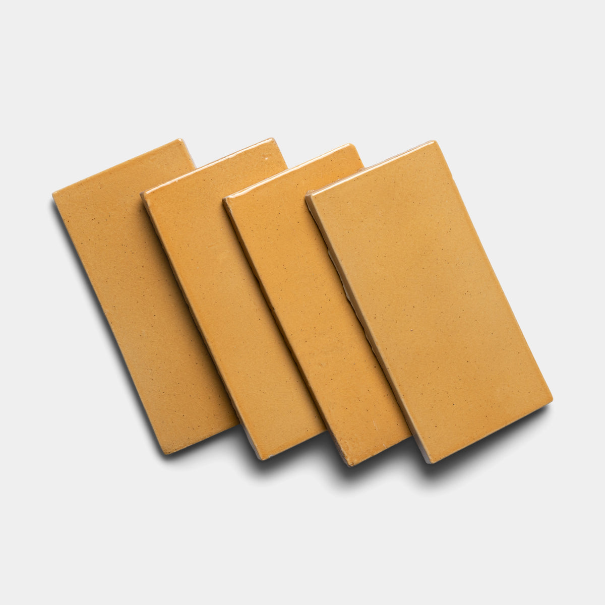 Four Dorado 4x8 Rectangle tiles by Zia Tile are arranged in a slightly overlapped, diagonal row on a white background, casting soft shadows to the right.