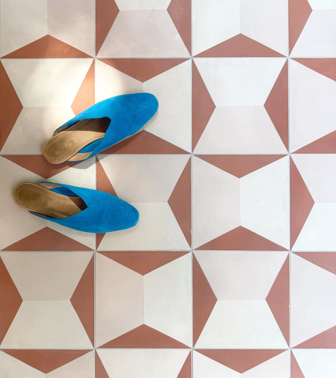 A pair of bright blue slip-on shoes on a geometric-patterned floor with Zia Tile’s Colorama Dune 8x8 handmade tiles in white and terracotta triangles and hexagons.