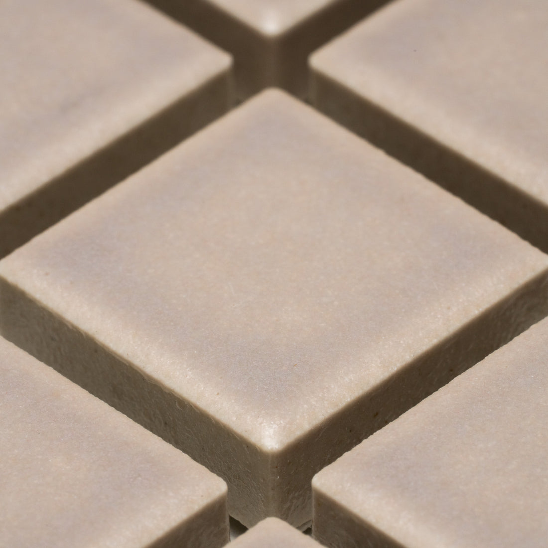 Close-up view of several smooth, beige Earl Grey 1x1 tiles by Zia Tile, arranged in a grid pattern with visible grout lines separating each square tile.