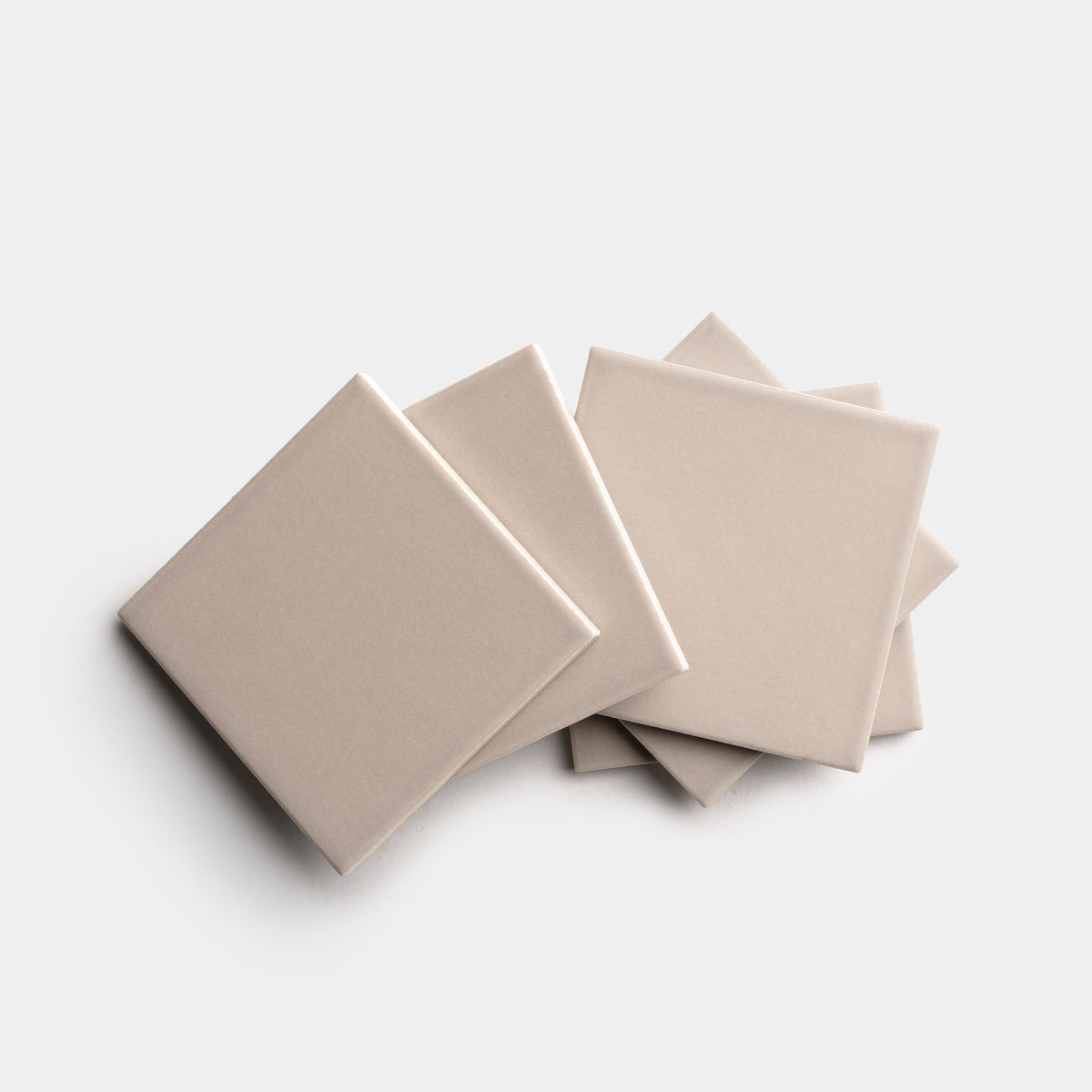 Four Zia Tile Earl Grey 4x4 ceramic tiles in light beige are arranged in an overlapping, fanned-out pattern on a white background.