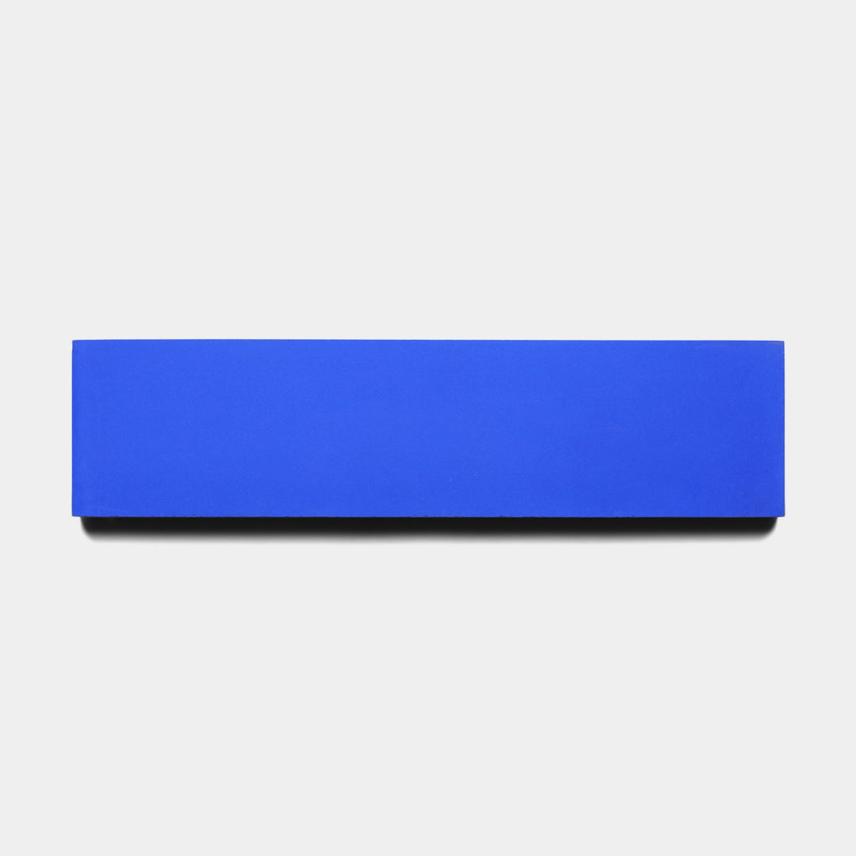 A Zia Tile Elemental Blue 2x8 sample with sharp edges sits centered on a plain white background, casting a faint shadow to showcase its clean design.