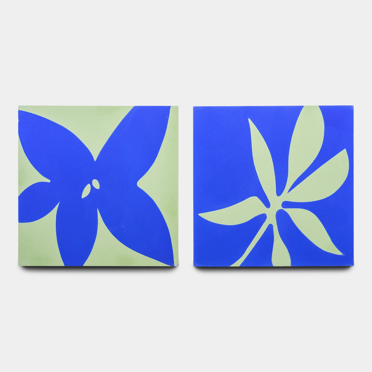 The Flora 8x8 Set Elemental Blue + Nile Sample by Zia Tile shows two square tiles with abstract floral designs: one has a blue flower on a green background, the other a green flower on blue.