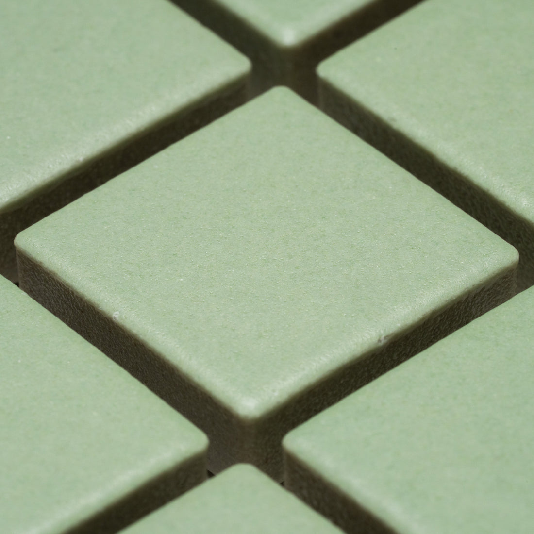 Close-up of Zia Tile's Eucalyptus 1x1 green square tiles arranged in a grid, featuring visible gaps and a textured surface.