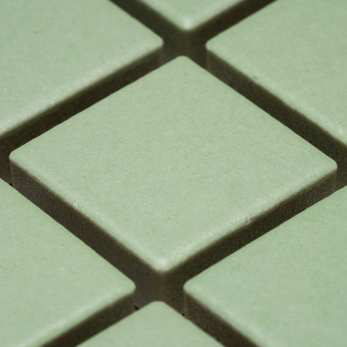 Close-up of Zia Tile's Eucalyptus 1x1 green square tiles arranged in a grid, featuring visible gaps and a textured surface.