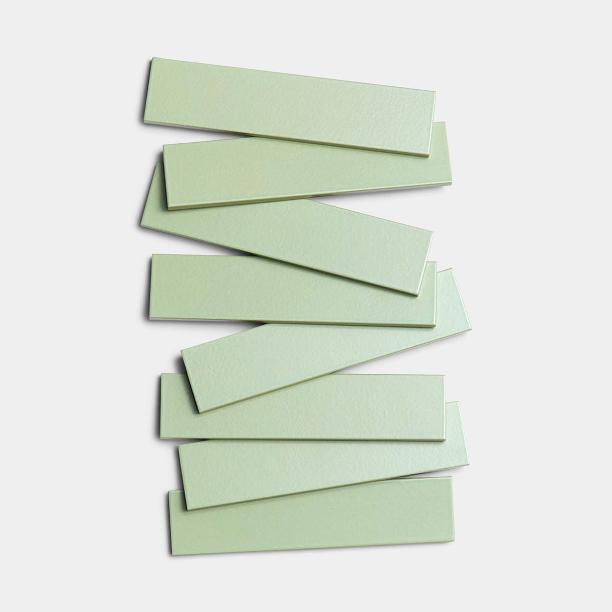Eight Eucalyptus 2x8 tiles by Zia Tile, in light green architectural grade ceramic, are stacked in a slightly staggered pile against a white background.